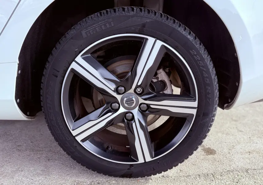 Gros plan sur la roue avant droite d'une Volvo V40 blanche, jante alliage R-Design à cinq branches noires et argentées.