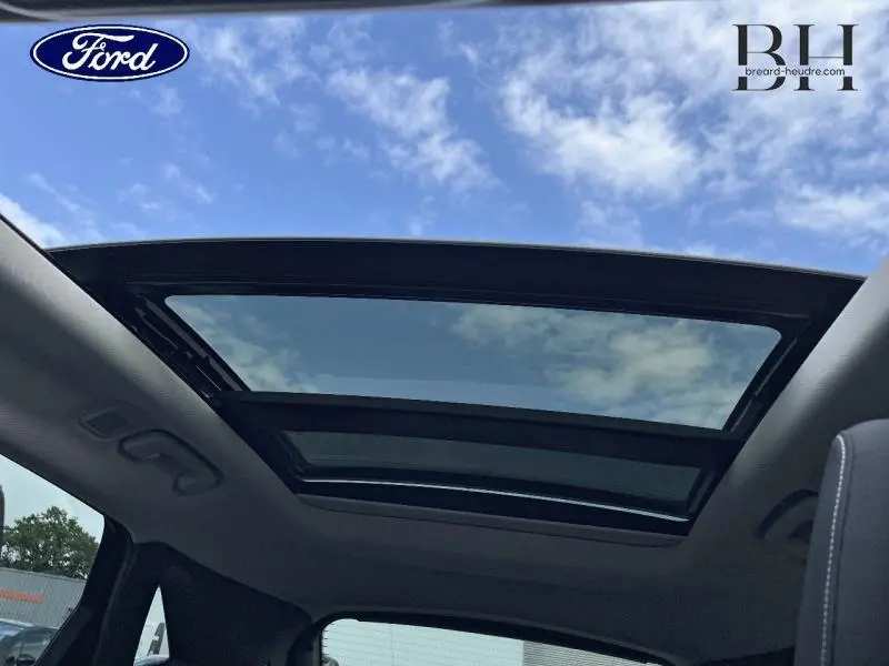 Toit panoramique ouvert du Ford Kuga 2022 en Premium Rouge Lucid, vue intérieure vers le ciel bleu.