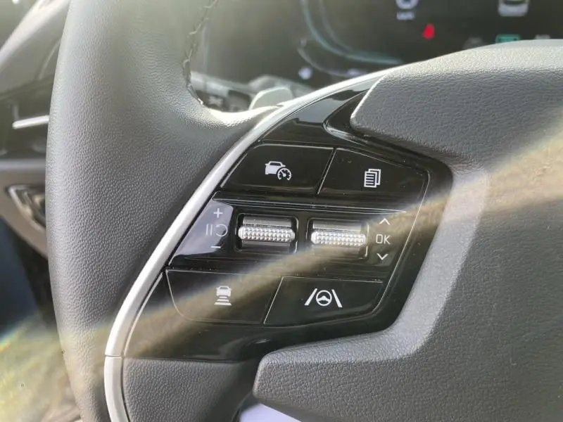 Gros plan sur les commandes du volant côté gauche du KIA NIRO 2024 bleu métal, avec boutons de régulateur et assistances.