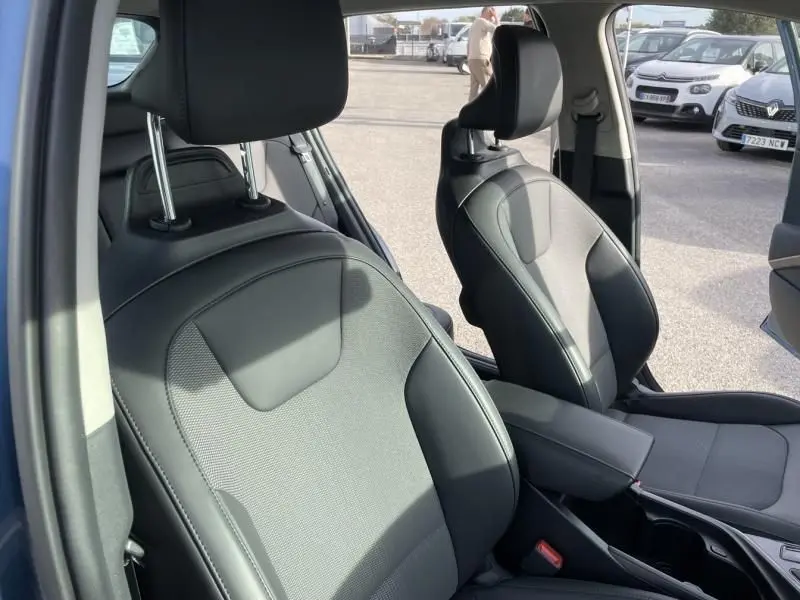 Intérieur du Kia Niro 2024 bleu métal, vue rapprochée des sièges avant en tissu et cuir noir, côté conducteur et passager.