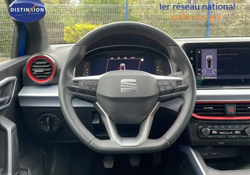 Vue intérieure centrée sur le volant perforé de la SEAT Arona 2025 avec détails rouges et tableau de bord numérique.