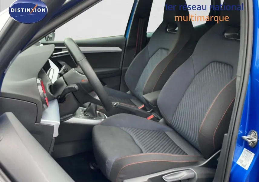 Vue intérieure côté gauche du SEAT Arona bleu saphir, montrant les sièges sport noirs avec surpiqûres orange et volant multifonction.