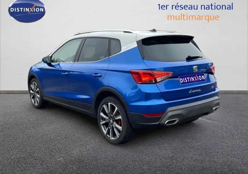 Vue 3/4 arrière gauche d’un SEAT Arona bleu saphir métal avec toit blanc, jantes alliage et feux arrière LED.