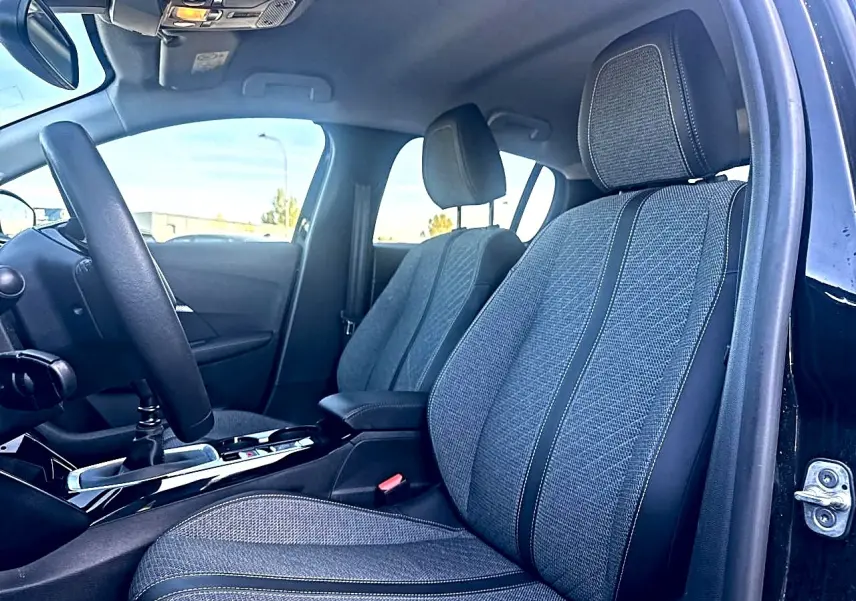 Intérieur de la Peugeot 208 1.2 100 Allure noir, vue côté conducteur sur les sièges en tissu gris et volant.