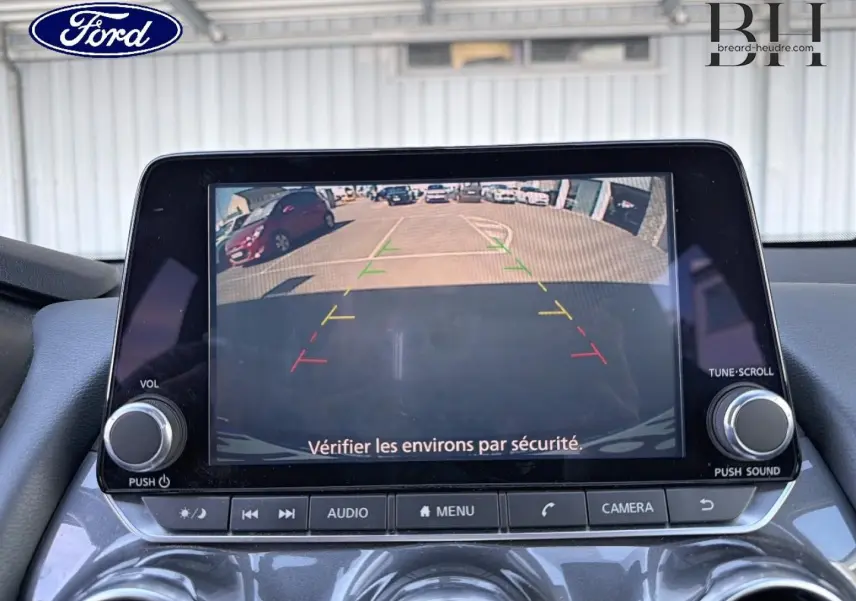 Écran tactile intérieur montrant la caméra de recul d'une Nissan Juke noir métallisé, avec commandes audio visibles.