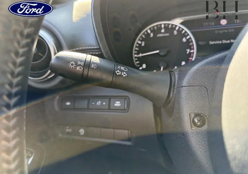 Gros plan sur la manette de clignotants noire à gauche du volant dans l'habitacle d'une Nissan Juke noir métallisé.