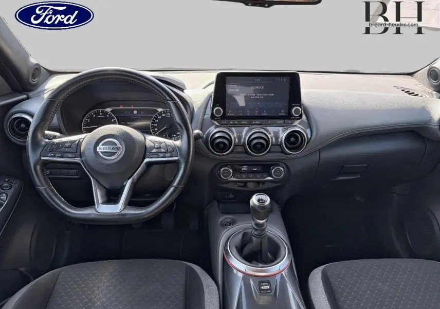 Vue intérieure avant du Nissan Juke 2020 avec volant cuir multifonction et écran tactile central, levier de vitesse manuel visible.