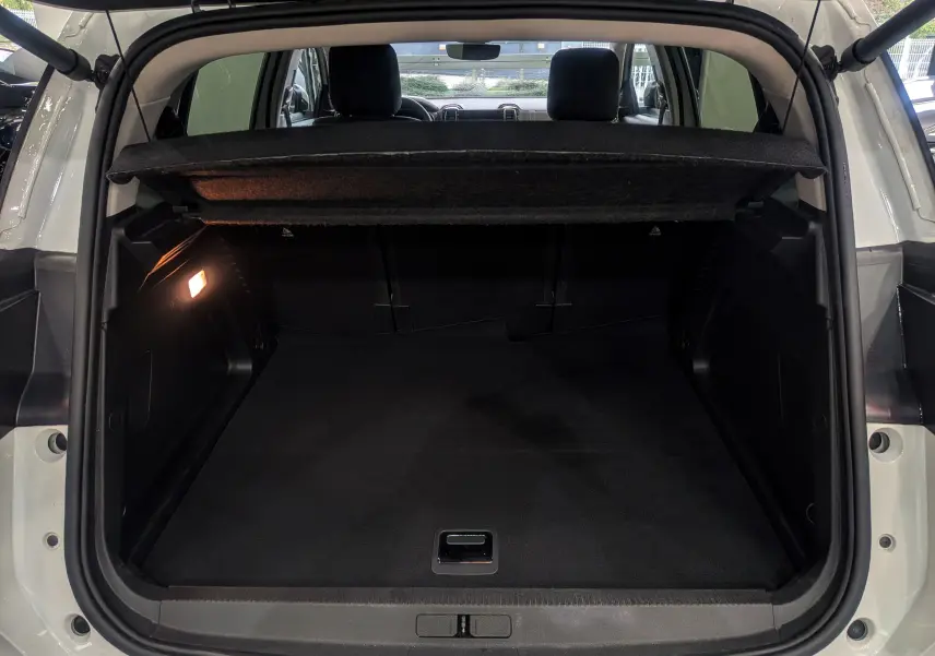 Coffre ouvert vu de l'arrière d'un Citroën C5 Aircross blanc Glacier avec cache-bagages et lumière intérieure allumée.