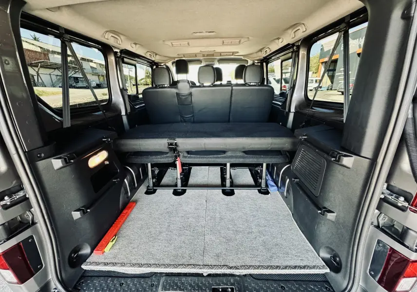 Vue arrière de l’intérieur gris et noir du Nissan NV300 Combi 9 places avec banquette rabattue et espace de chargement.