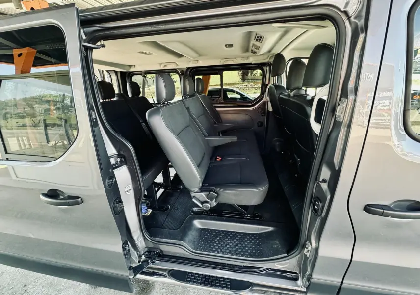 Vue latérale intérieure du Nissan NV300 Combi gris, montrant les sièges en tissu noir et la porte coulissante ouverte.