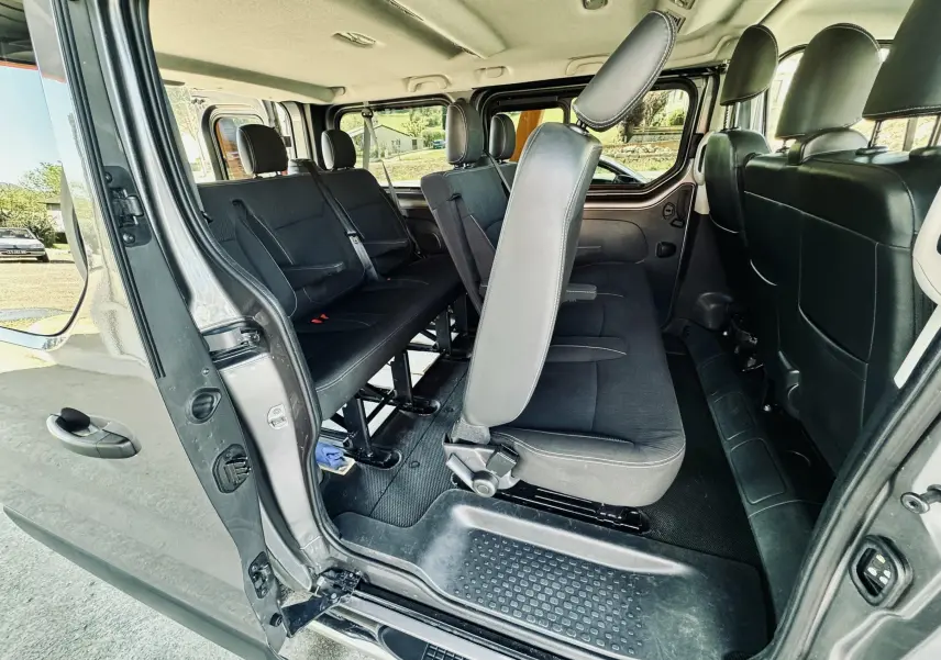 Vue intérieure côté droit du Nissan NV300 Combi gris, montrant les sièges en tissu noir et l'espace passagers.