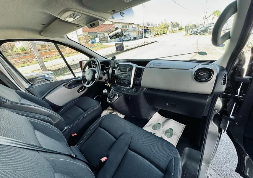 Vue intérieure côté conducteur du Nissan NV300 Combi gris, montrant le tableau de bord et les sièges en tissu noir.