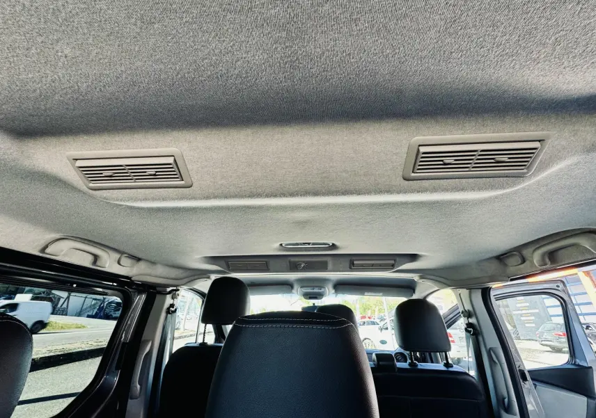 Vue intérieure du toit gris avec bouches d'aération, sièges noirs et portières ouvertes du Nissan NV300 Combi.