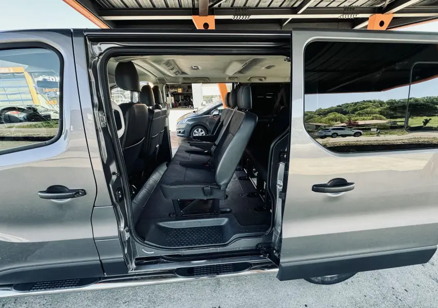 Vue latérale droite d’un Nissan NV300 Combi gris 2018 avec porte coulissante ouverte montrant les sièges passagers en tissu noir.