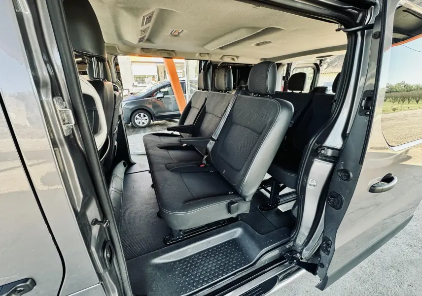 Vue intérieure côté droit du Nissan NV300 Combi gris, montrant les sièges passagers en tissu noir et l'ouverture de la porte coulissante.