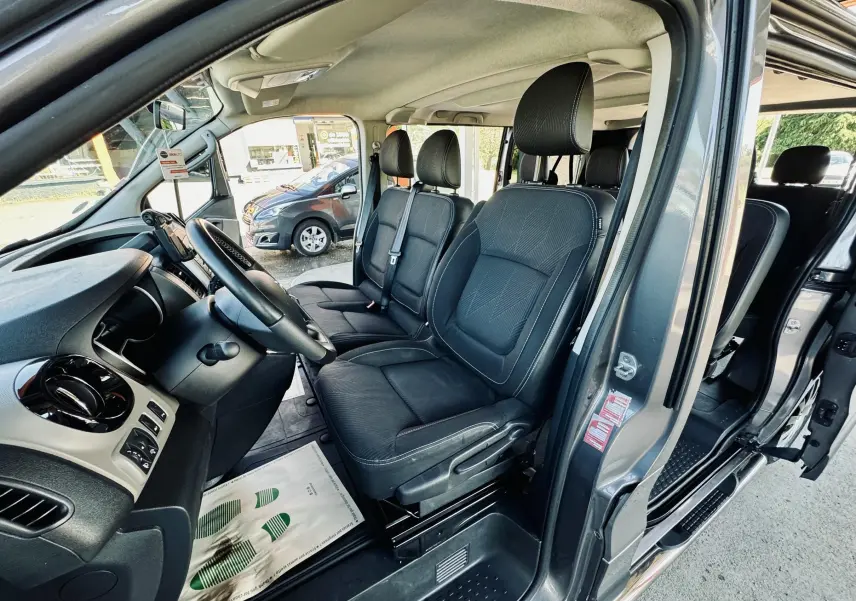 Vue intérieure côté conducteur du Nissan NV300 Combi gris, montrant les sièges avant en tissu noir et le tableau de bord.