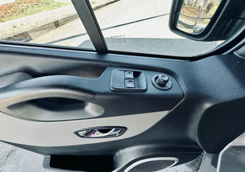 Vue intérieure côté conducteur de la porte gris clair et noir du Nissan NV300 Combi avec commandes de vitres et rétroviseur.