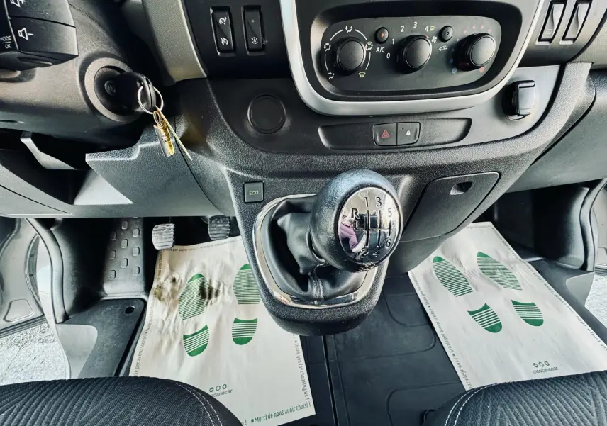 Vue intérieure centrée sur le levier de vitesse manuel et les commandes de climatisation du Nissan NV300 Combi gris.