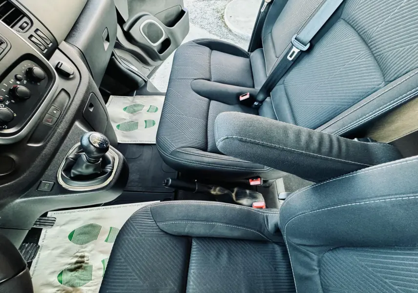 Vue intérieure côté conducteur du Nissan NV300 Combi 2018, sièges tissu gris foncé avec accoudoirs et levier de vitesse manuel.