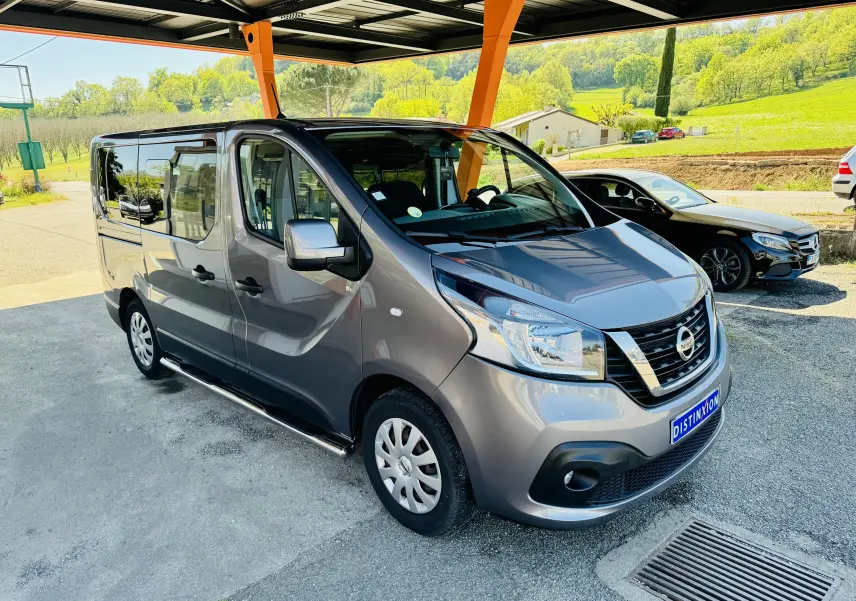 Nissan NV300 Combi gris en vue 3/4 avant droit sous abri avec paysage verdoyant en arrière-plan.