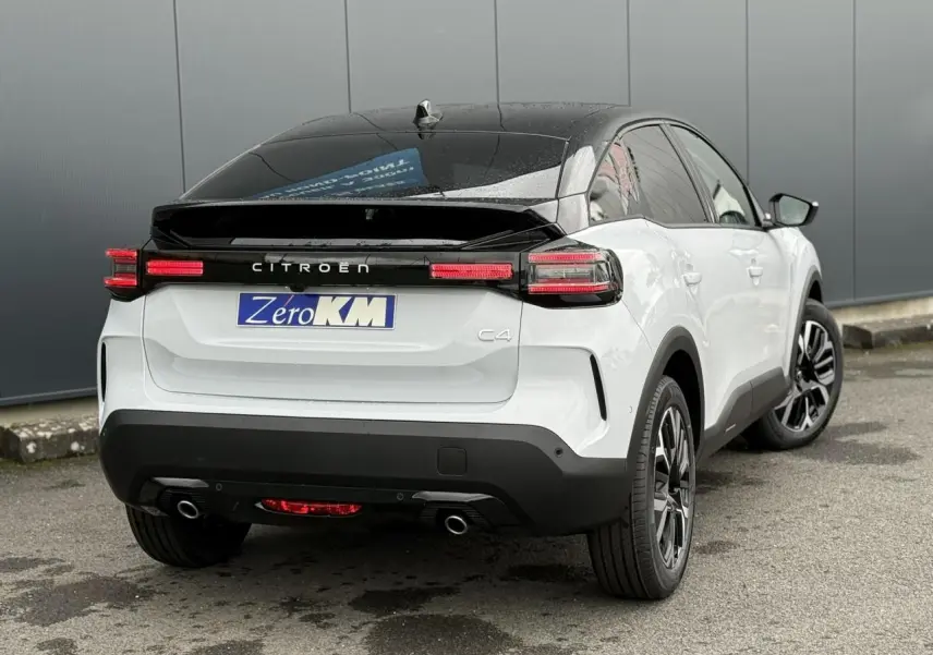 Vue 3/4 arrière droite d'une Citroën C4 hybride blanche avec toit noir et feux arrière LED allumés.