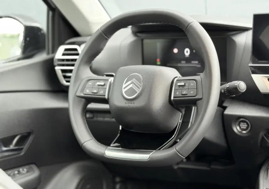 Volant cuir noir avec commandes intégrées et logo Citroën, vue rapprochée de l'habitacle avant du C4 hybride 2025.
