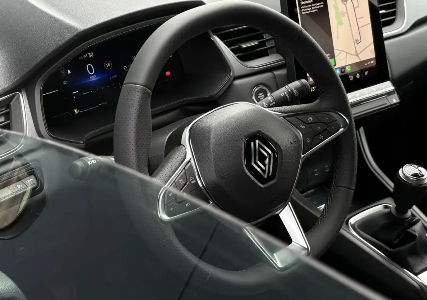 Vue rapprochée du volant noir perforé et du levier de vitesses manuel du Renault Captur 2025 avec écran tactile vertical.