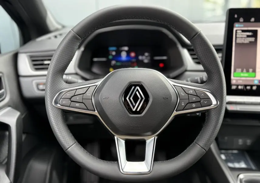 Volant en cuir noir perforé de Renault Captur 2025 avec commandes intégrées et tableau de bord numérique flou en arrière-plan.