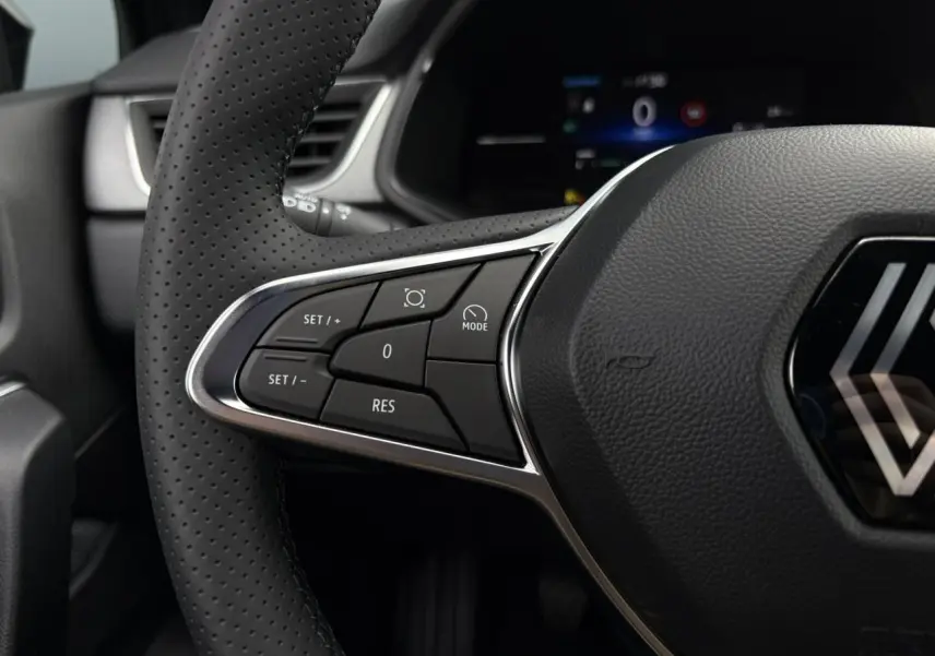 Gros plan sur le volant perforé du Renault Captur Noir Étoile 2025 avec commandes intégrées et logo central visible.