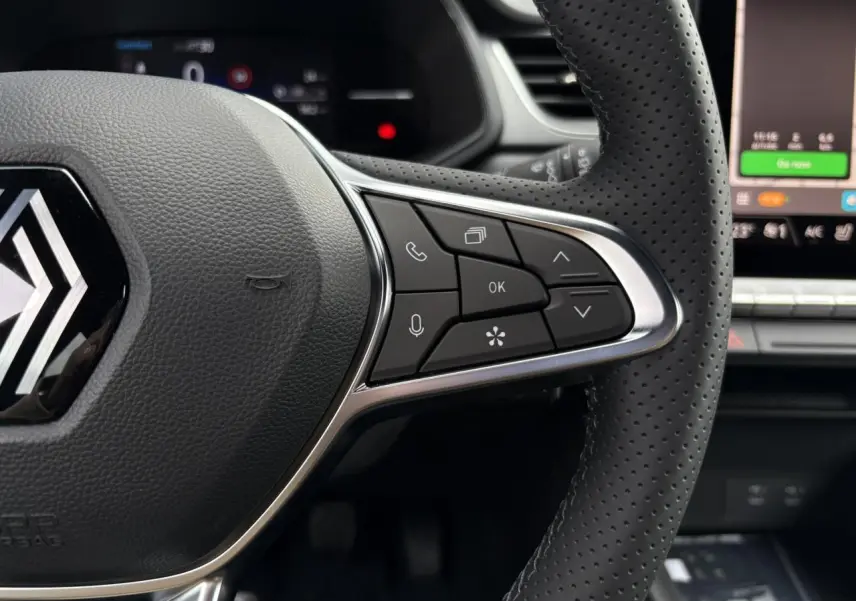 Gros plan sur le volant noir perforé du Renault Captur 2025 avec commandes multifonctions et écran tactile en arrière-plan.