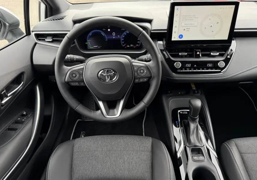 Vue intérieure frontale du poste de conduite de la Toyota Corolla Touring Sport 2025, avec volant multifonction et écran tactile central.