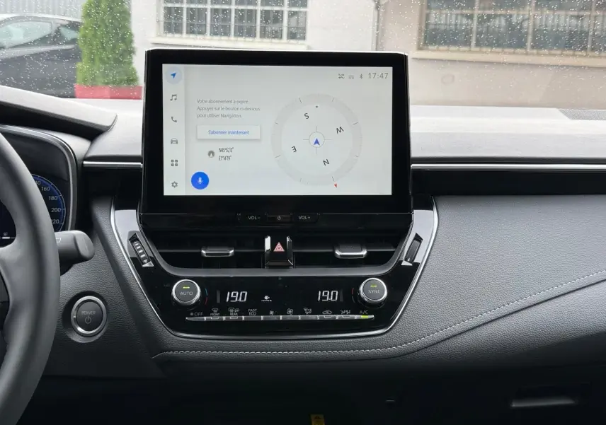 Tableau de bord de Toyota Corolla Touring Sport 2025 avec écran tactile central affichant une boussole et commandes climatisation.