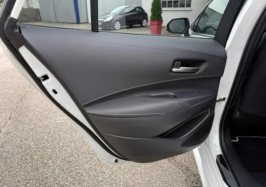 Vue rapprochée de la porte arrière droite noire avec surpiqûres blanches de la Toyota Corolla Touring Sport blanche lunaire nacrée.