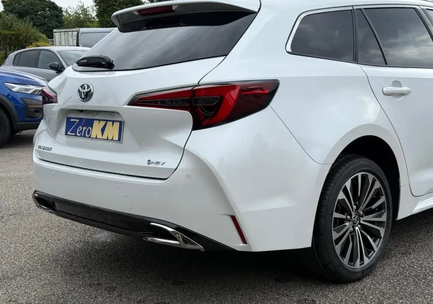 Vue 3/4 arrière droite d'une Toyota Corolla Touring Sport blanche nacrée avec feux arrière LED et jantes alliage noires.