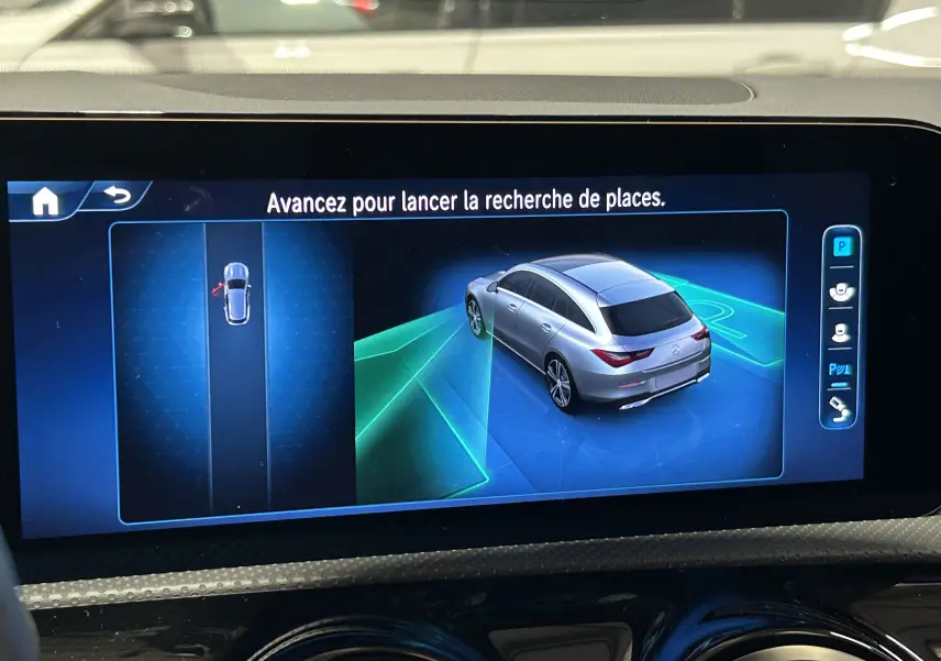 Affichage écran multimédia montrant une vue 3/4 arrière argentée d'une Mercedes CLA Shooting Brake II en stationnement assisté.