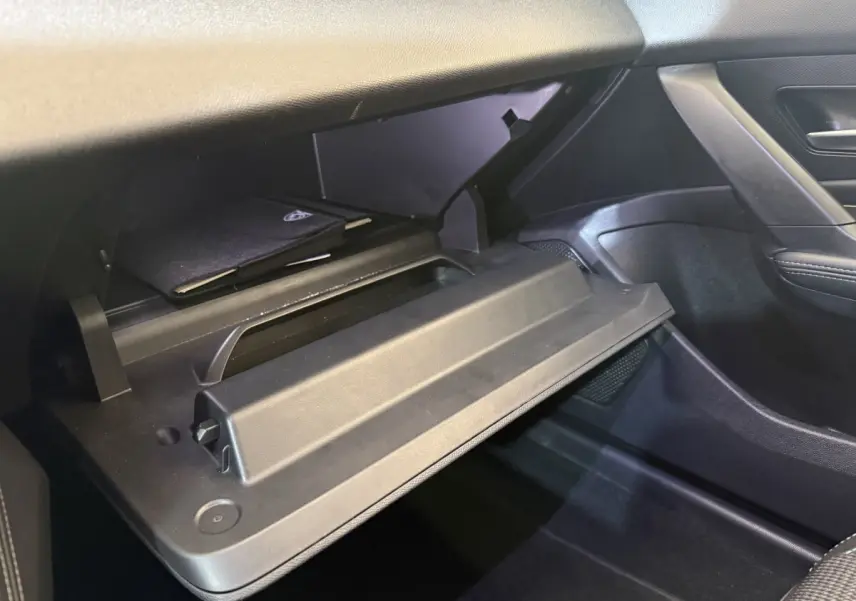 Vue intérieure côté passager de la boîte à gants ouverte de la Peugeot 308 gris foncé, avec rangement et manuel visible.