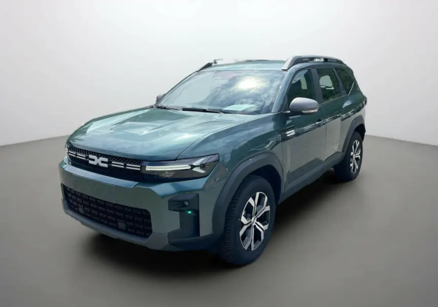 SUV Dacia Bigster vert cèdre en 3/4 avant droit, avec barres de toit et jantes alu 17 pouces visibles.