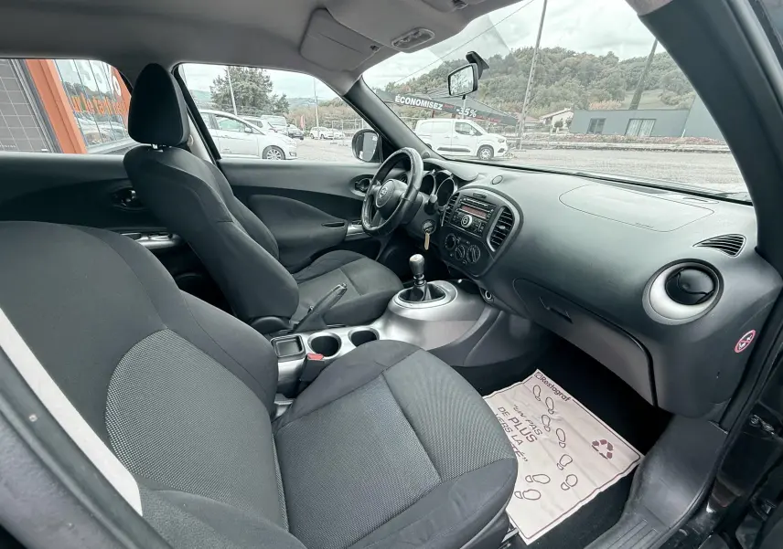 Intérieur noir du Nissan Juke 2012 vu côté passager, montrant sièges en tissu et tableau de bord avec boîte manuelle.