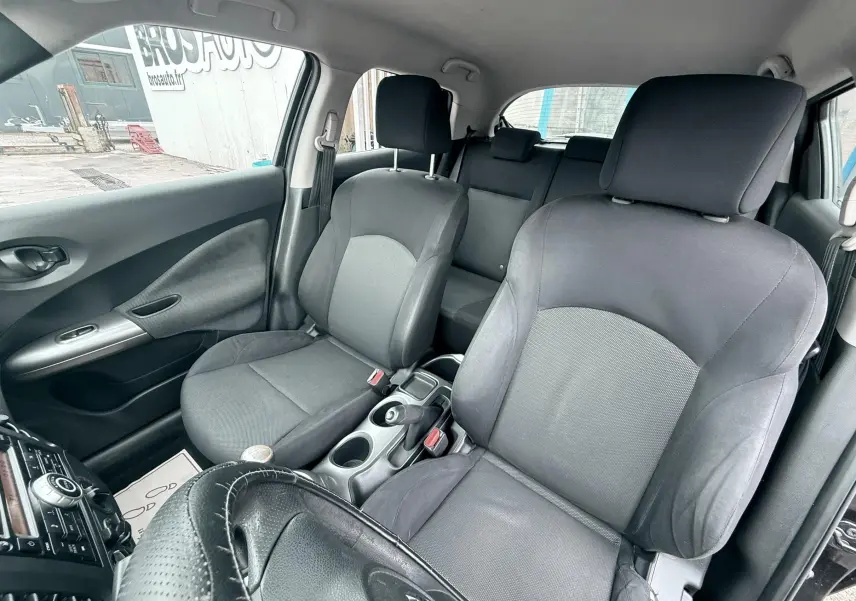 Vue intérieure côté avant droit du Nissan Juke 2012 noir, montrant les sièges en tissu et cuir ainsi que la console centrale.