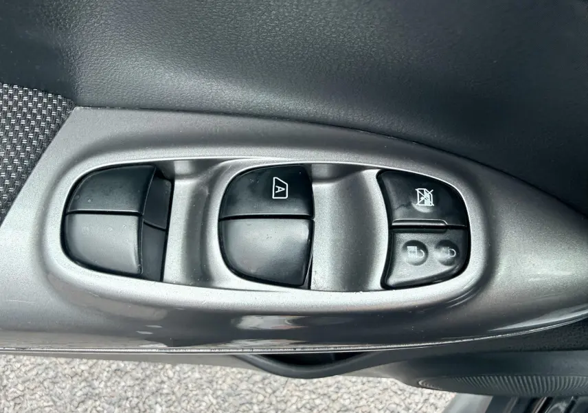 Gros plan sur les commandes des vitres électriques côté conducteur d’un Nissan Juke noir de 2012.