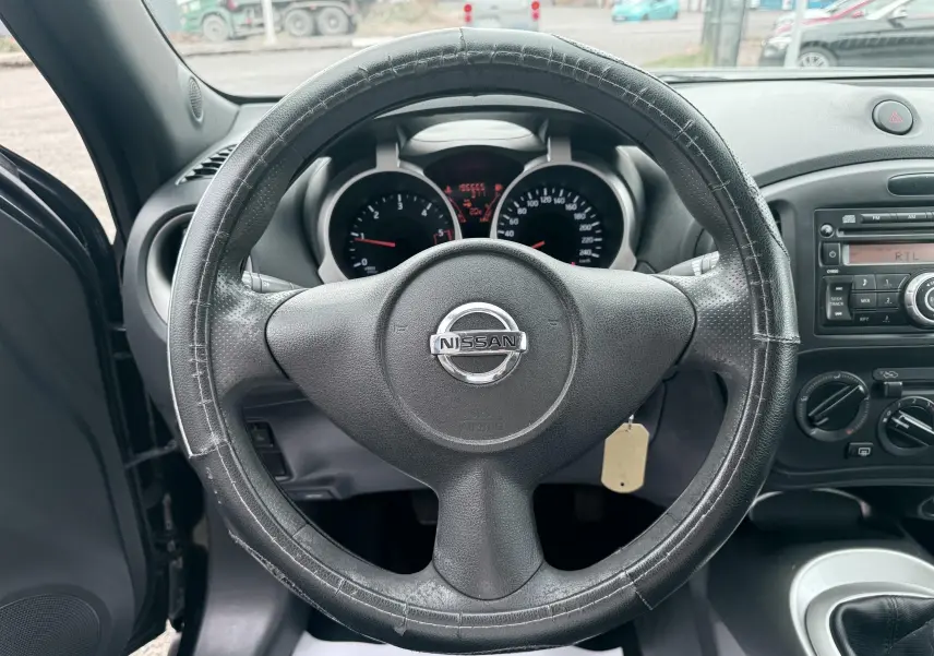 Vue centrée sur le volant noir usé d’un Nissan Juke 2012, avec tableau de bord et console radio visibles.