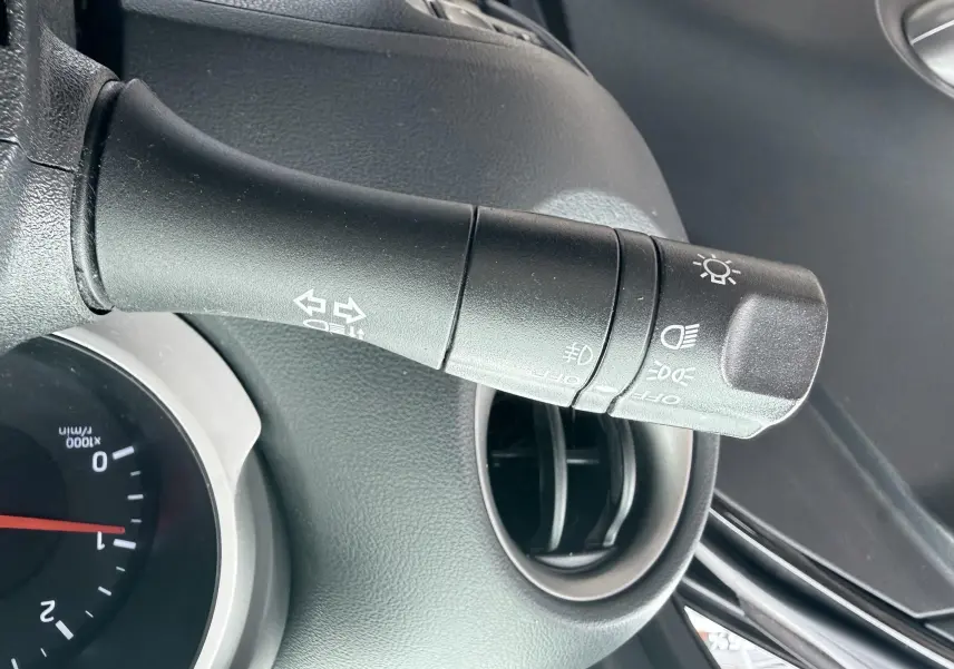 Gros plan sur la commande des phares et clignotants dans l’habitacle noir d’un Nissan Juke 2012.