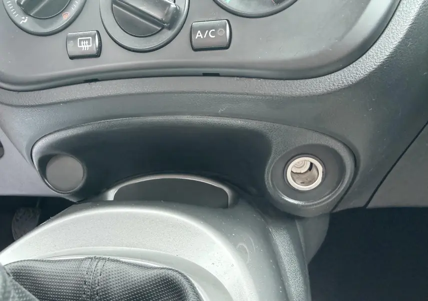 Détail de la console centrale noire du Nissan Juke 2012 montrant les commandes de climatisation et l’allume-cigare.
