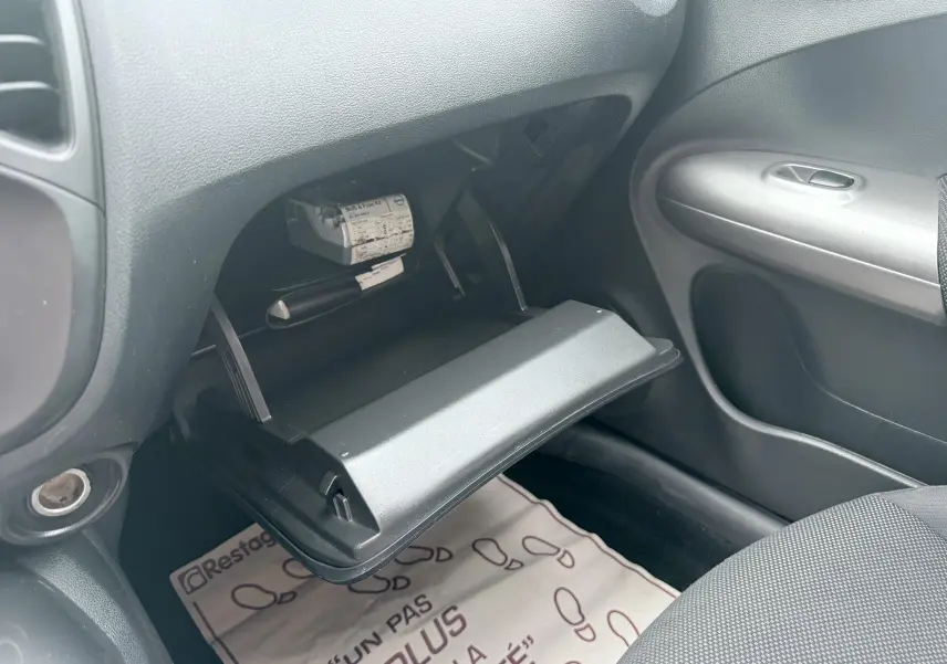 Intérieur côté passager du Nissan Juke 2012, boîte à gants ouverte avec tableau de bord et porte en tissu noir visibles.