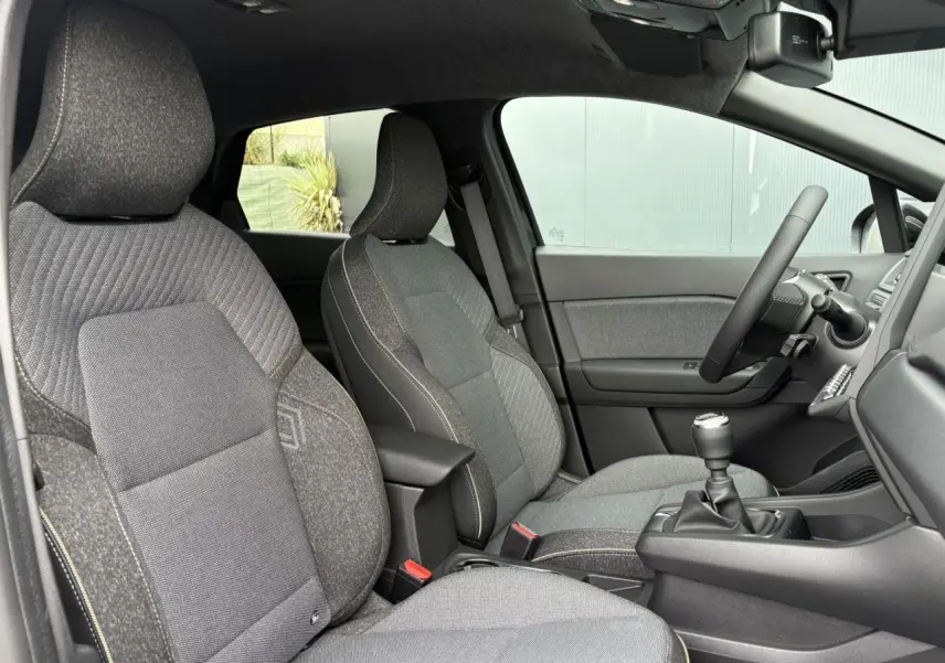 Vue intérieure côté gauche du Renault Captur 2025, sièges gris texturés et volant avec levier de vitesses manuel.