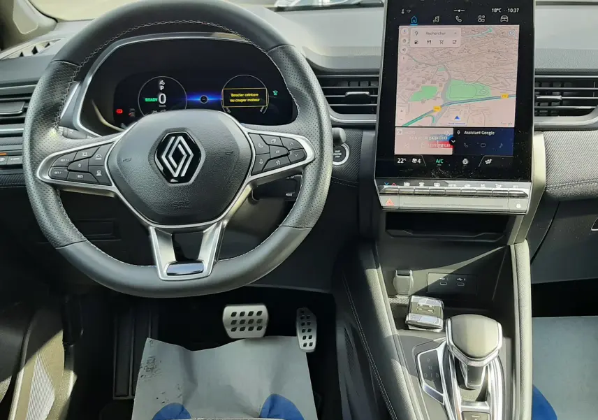 Intérieur du Renault Captur 2024, vue du poste de conduite avec volant multifonction et écran tactile central allumé.