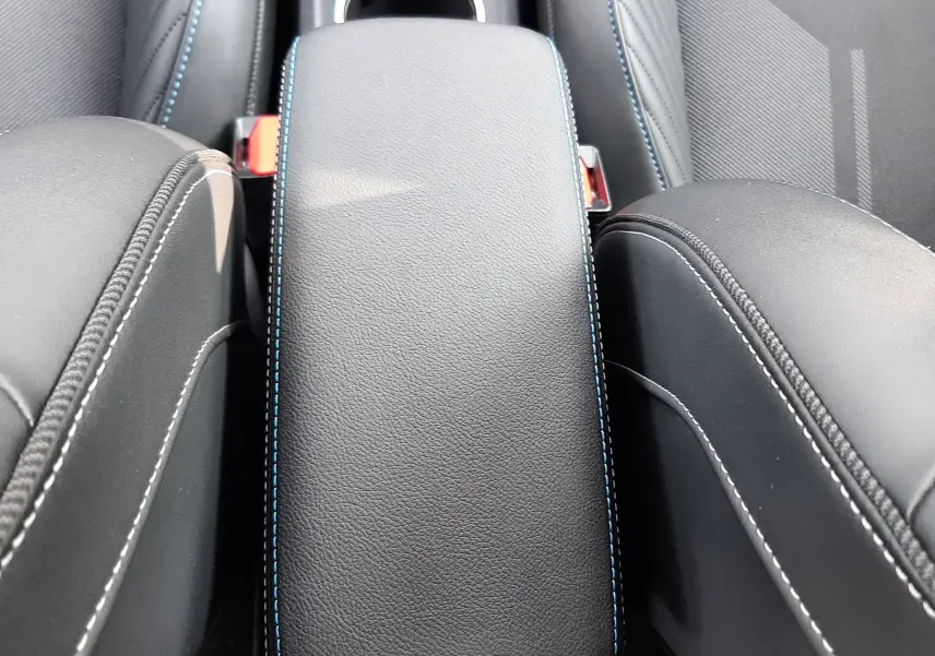 Accoudoir central en cuir noir avec surpiqûres bleues, entre les sièges avant du Renault Captur 2024 hybride.