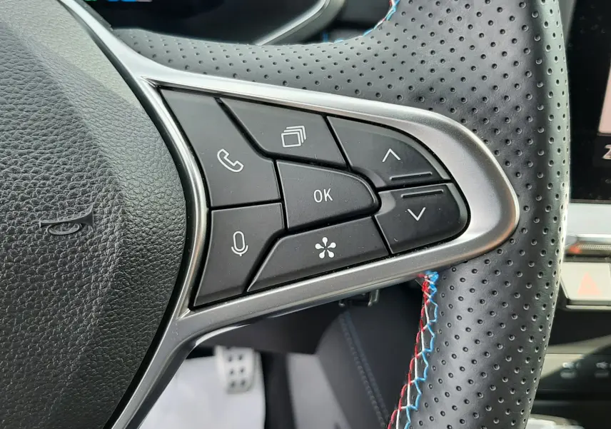 Gros plan sur les commandes du volant perforé avec surpiqûres tricolores du Renault Captur 2024 hybride.