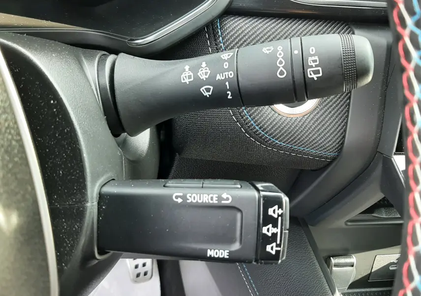 Gros plan sur les commandes de volant du Renault Captur 1.6 E-TECH hybride 2024, avec surpiqûres bleues et noir intérieur.