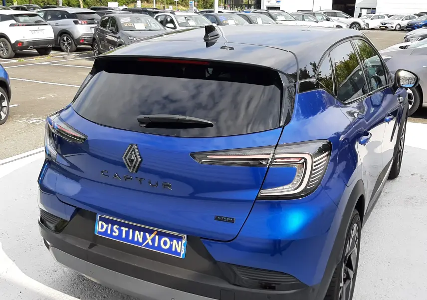 Vue 3/4 arrière droite d'un Renault Captur 2024 bleu Iron avec toit noir, feux LED et vitres teintées sur parking.